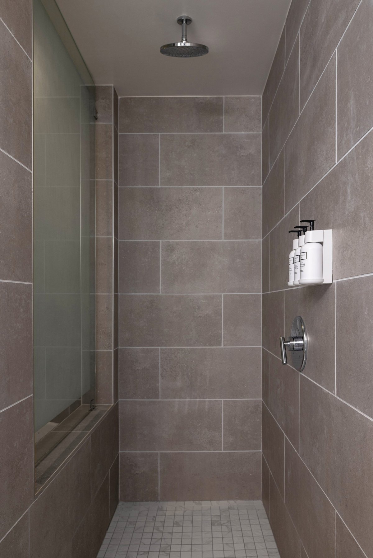 NK2 King with Jacuzzi — walk-in shower lined in warm grey tile with a ceiling-mounted rain head and wall-mounted amenity dispensers