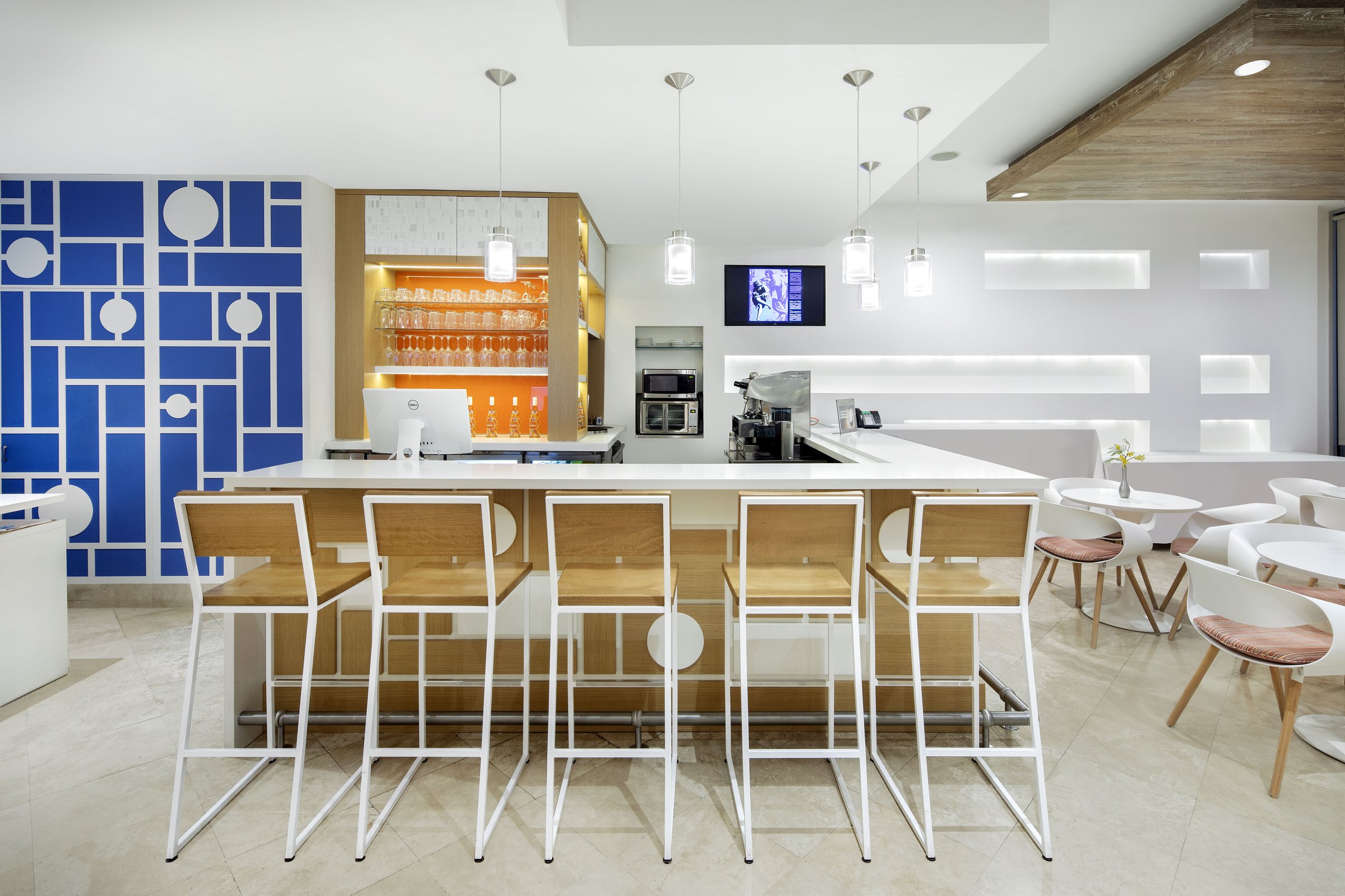Lobby cafe counter with wood-and-white bar stools set against a cobalt geometric mural