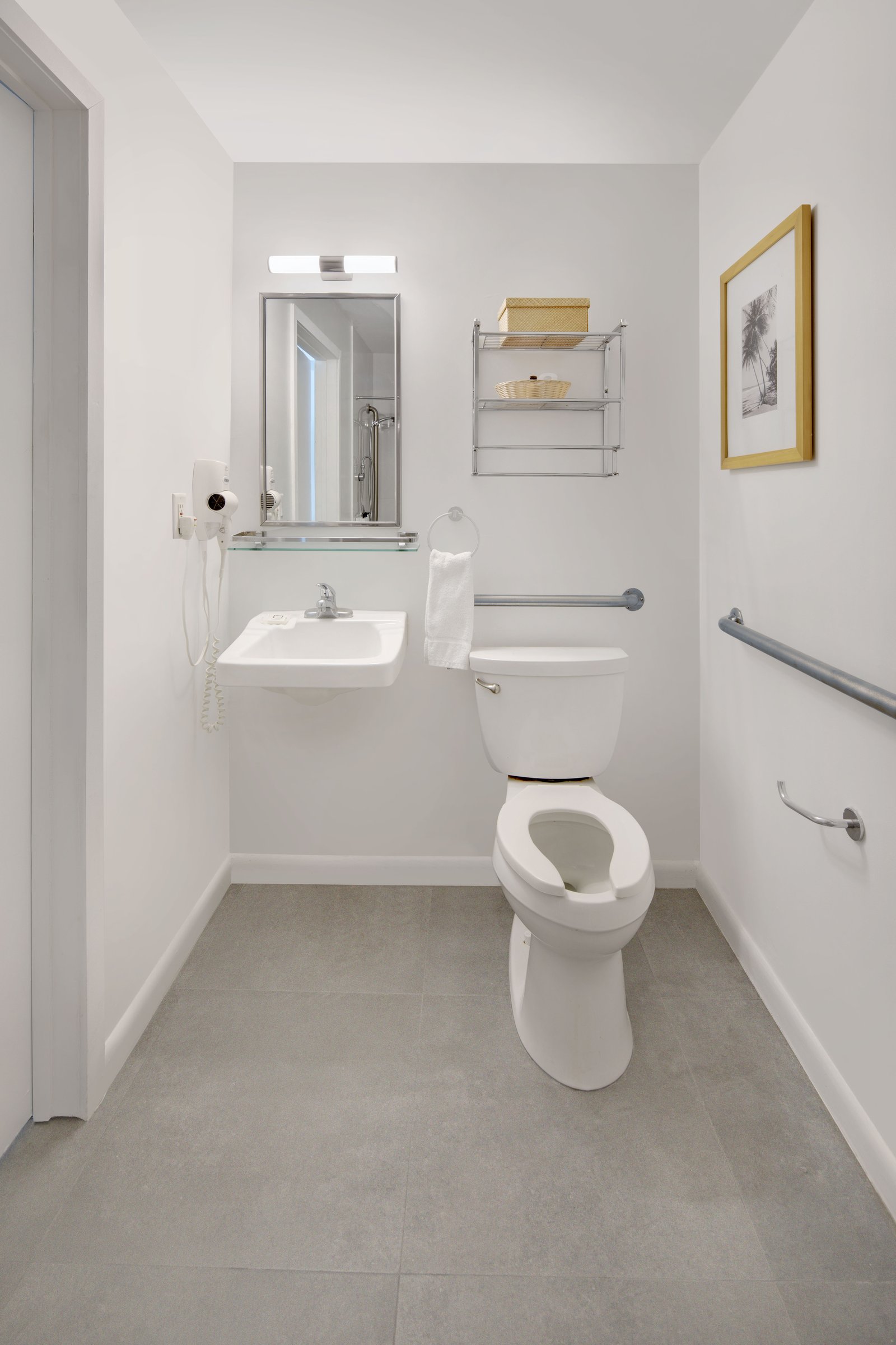 PNK1 accessible bathroom — wall-hung roll-under basin with a hairdryer, mirror and grab rails on two walls beside a raised-height toilet