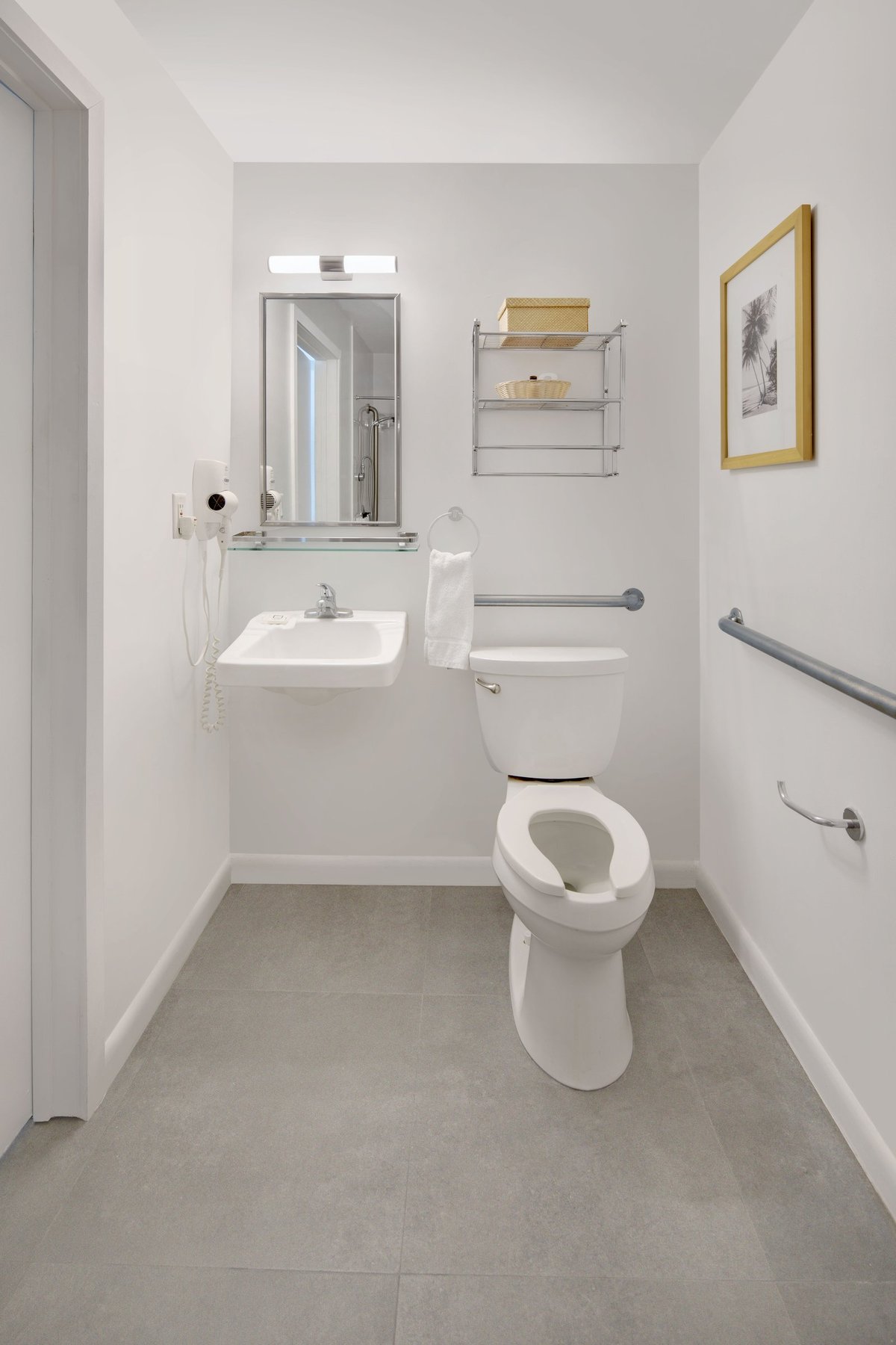 PNK1 accessible bathroom — wall-hung roll-under basin with a hairdryer, mirror and grab rails on two walls beside a raised-height toilet