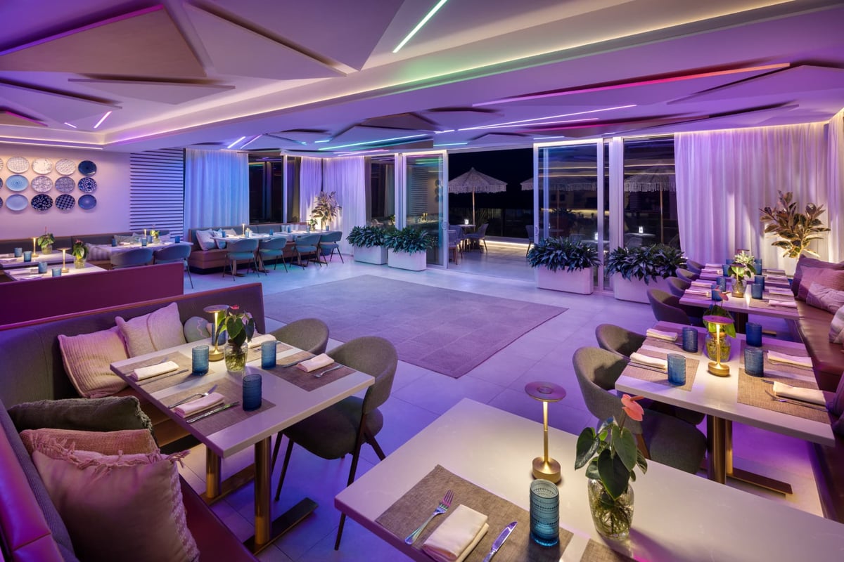 MB Hotel oceanfront event room at sunset — rows of blue-and-white bistro chairs facing floor-to-ceiling windows over the Atlantic