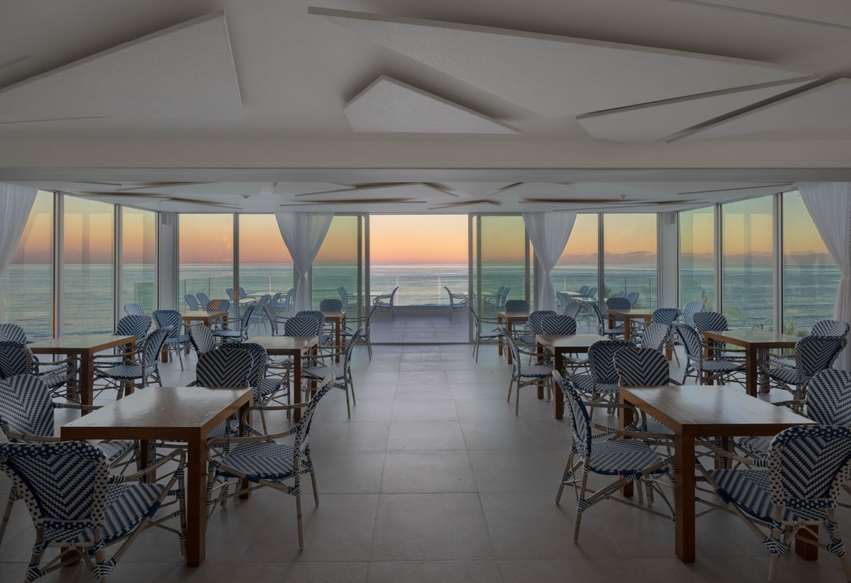 MB Hotel oceanfront event room at sunset, rows of blue-and-white bistro chairs facing floor-to-ceiling windows over the Atlantic