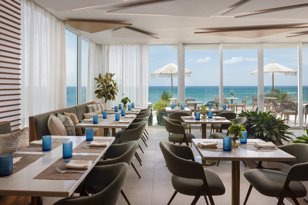 Kalypso dining room open to the pool deck at blue hour, lanterns set on every cane-chaired table