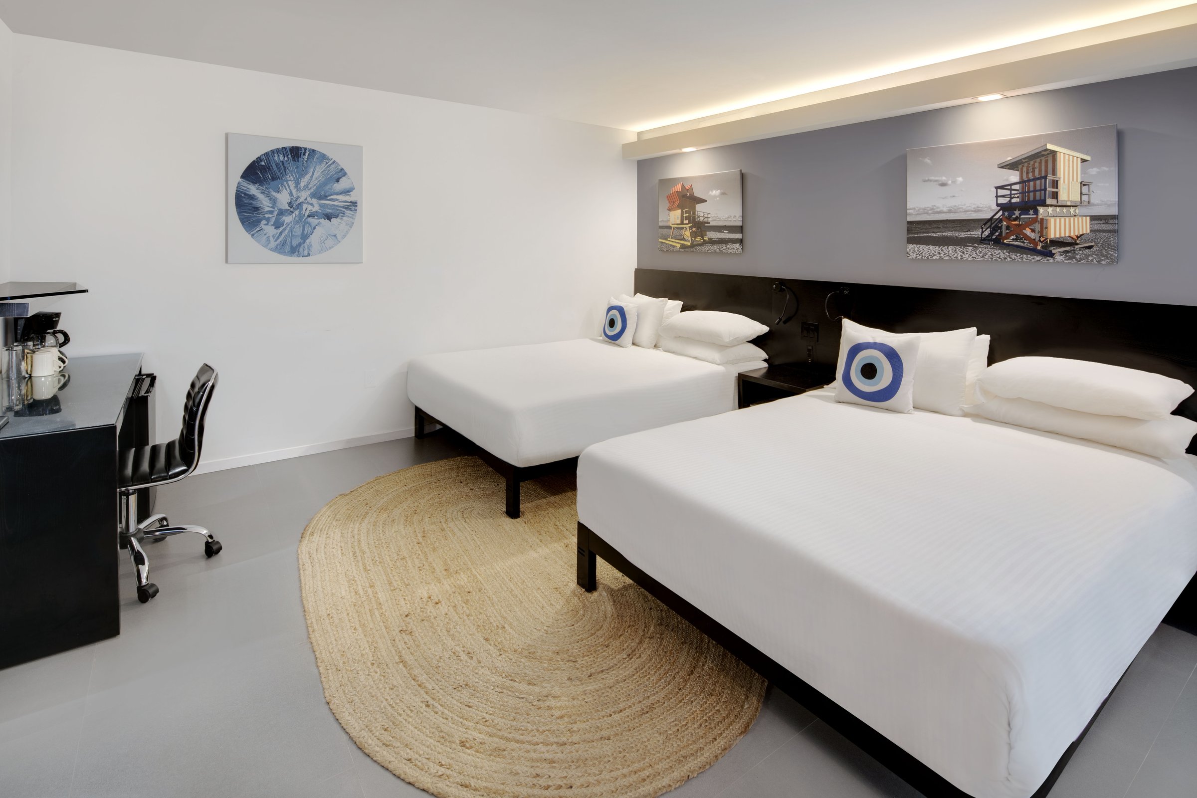 NQQ3 Superior Double Queen — the two queen beds seen from the entry, pale blue armchair and side table at the bright window, wall-mounted television opposite