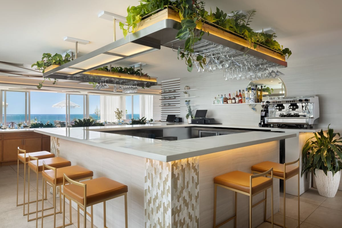 Kalypso oceanfront bar, brass-and-leather stools along a stone counter with the Atlantic through floor-to-ceiling glass
