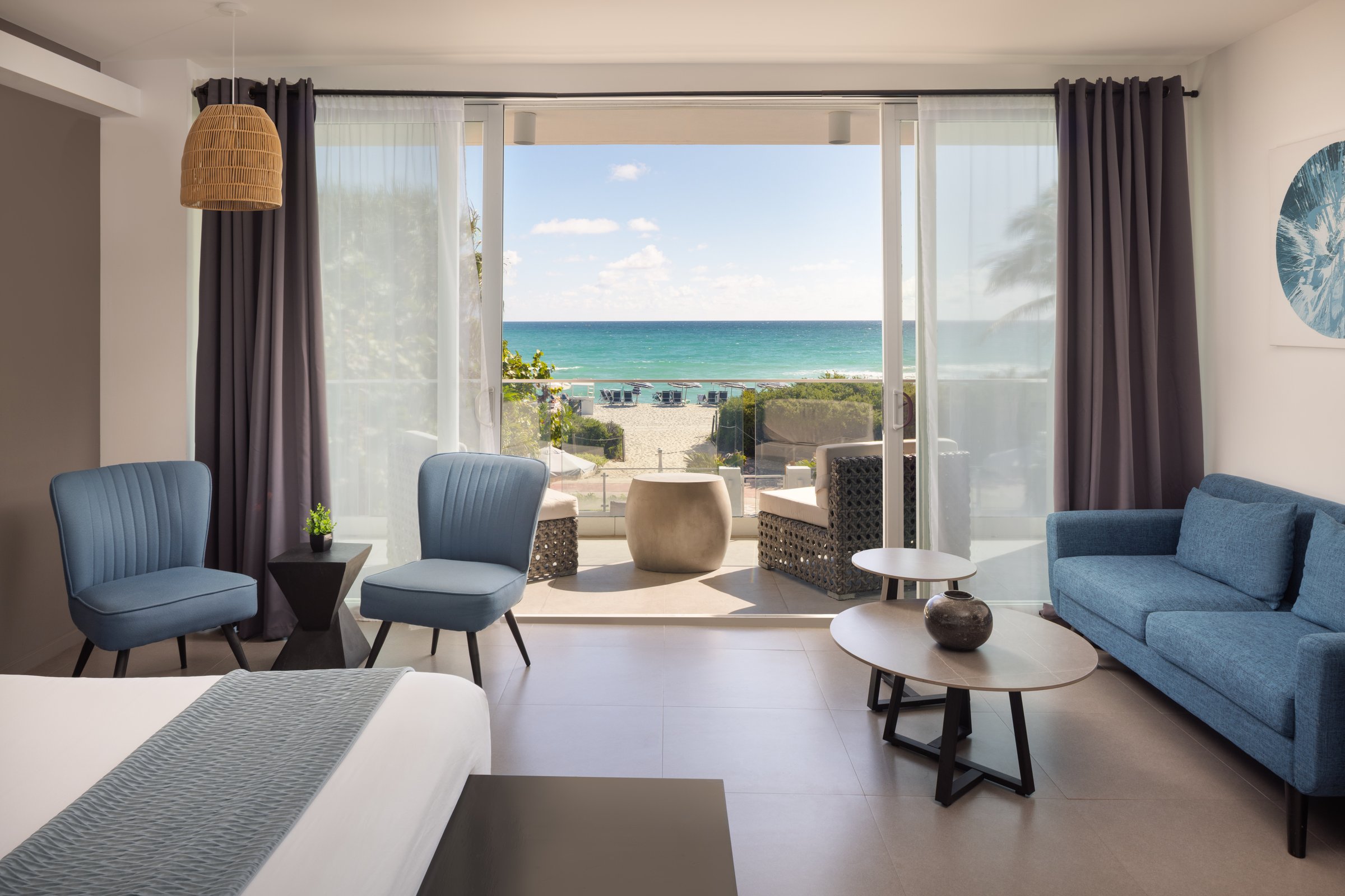 NK5 Deluxe Oceanfront King — bed facing open balcony doors, sand and turquoise water beyond