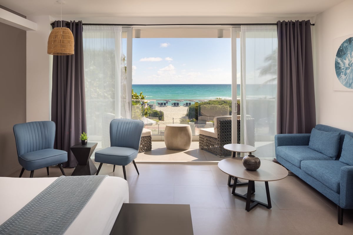 NK5 Deluxe Oceanfront King — sliding glass doors open onto a balcony with rattan loungers, sand and turquoise Atlantic water filling the view
