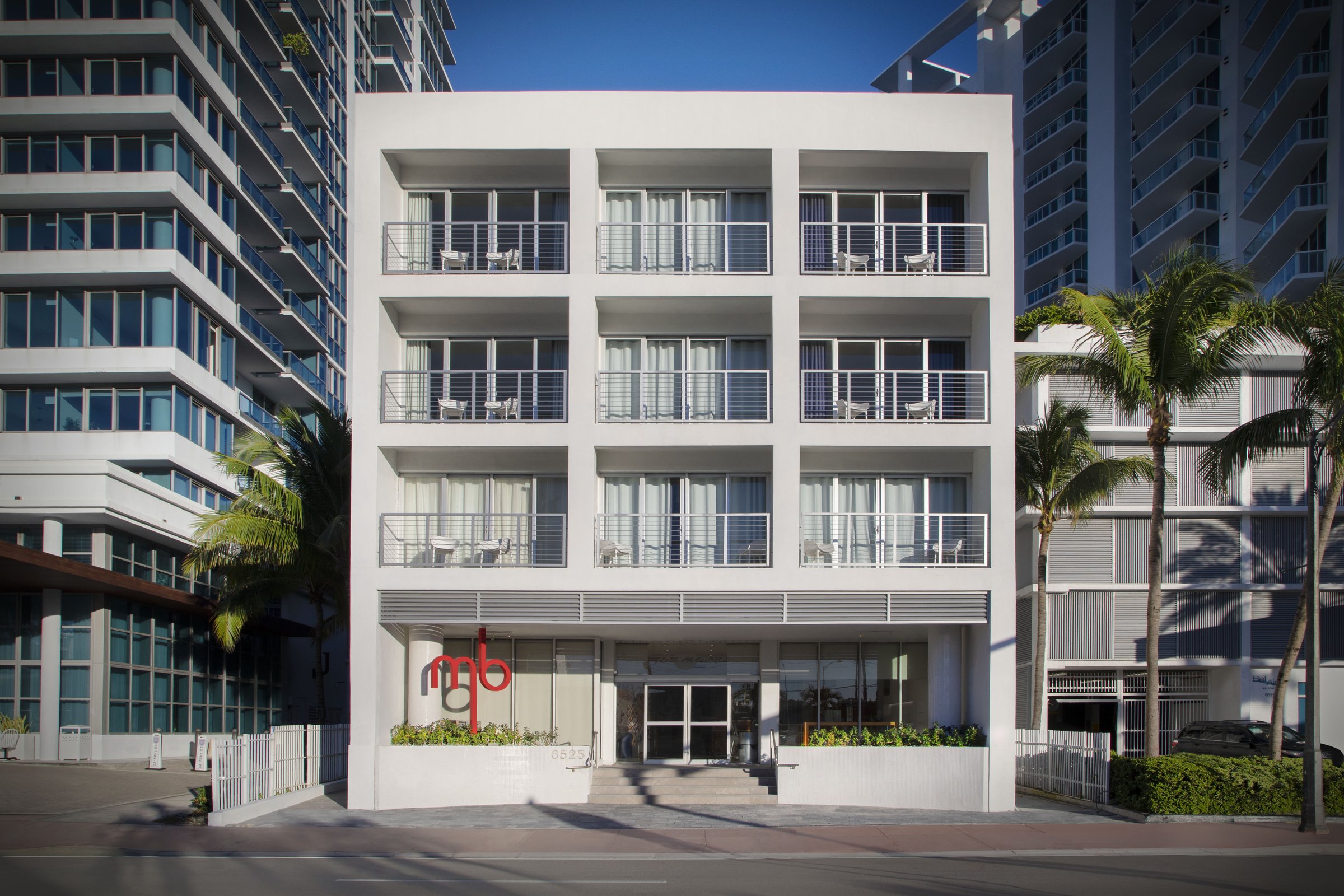 MB Hotel front facade in daylight, white balconies rising above the Collins Avenue entrance