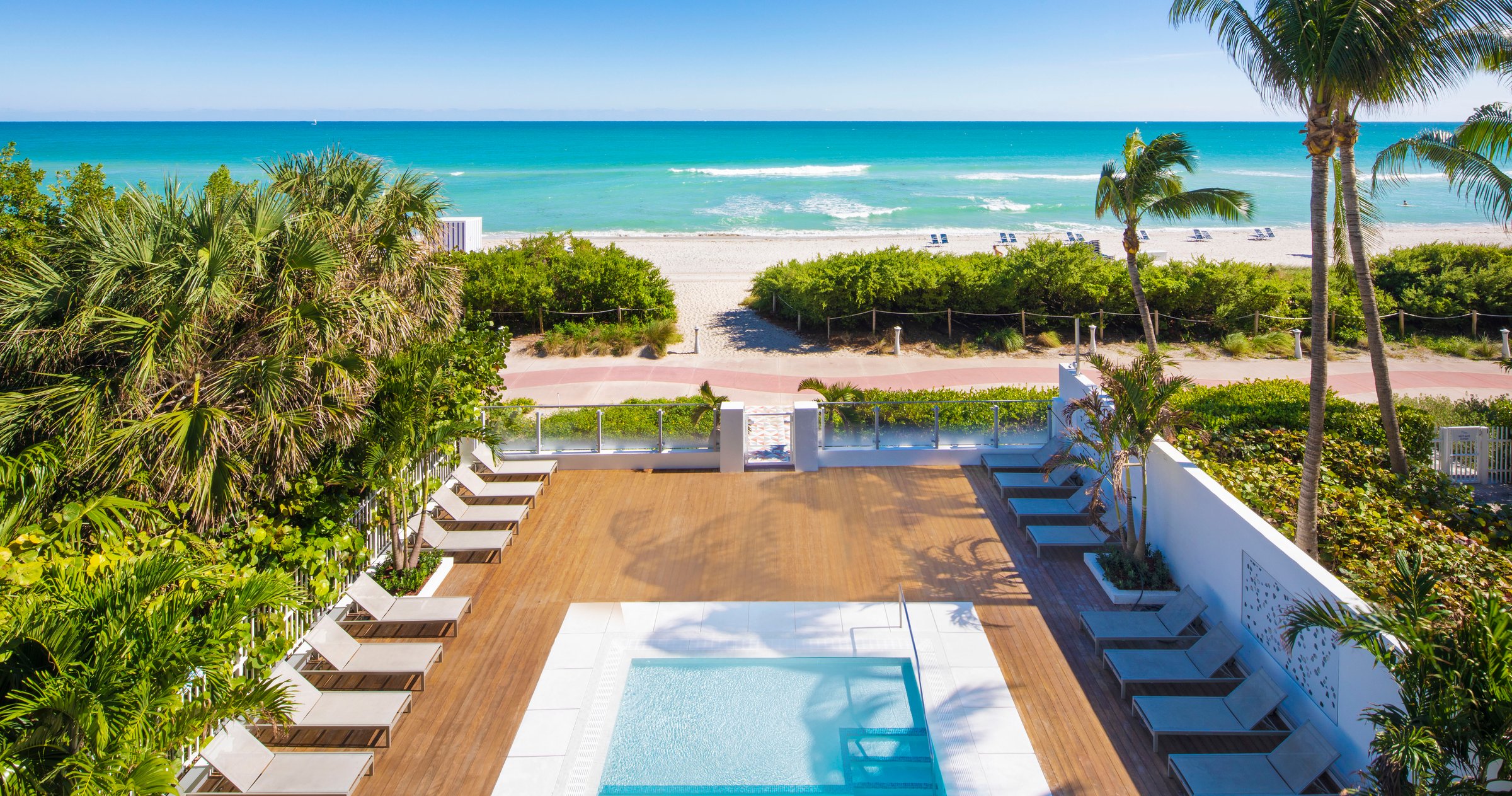 MB Hotel pool deck at golden hour, cream loungers and fringed umbrellas along the water with palms behind
