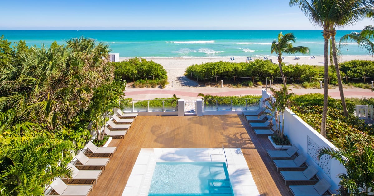 MB Hotel pool deck at golden hour, cream loungers and fringed umbrellas along the water with palms behind