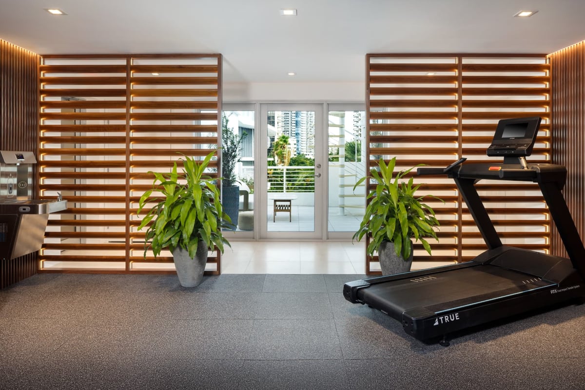 Fitness room with a TRUE treadmill, filtered water station and backlit teak slat screens opening to a planted terrace