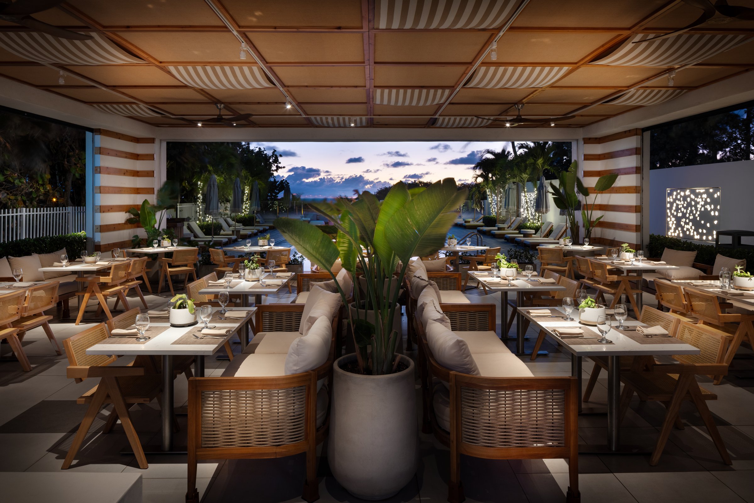 Kalypso restaurant open to the pool deck at blue hour, lanterns on cane-chaired tables