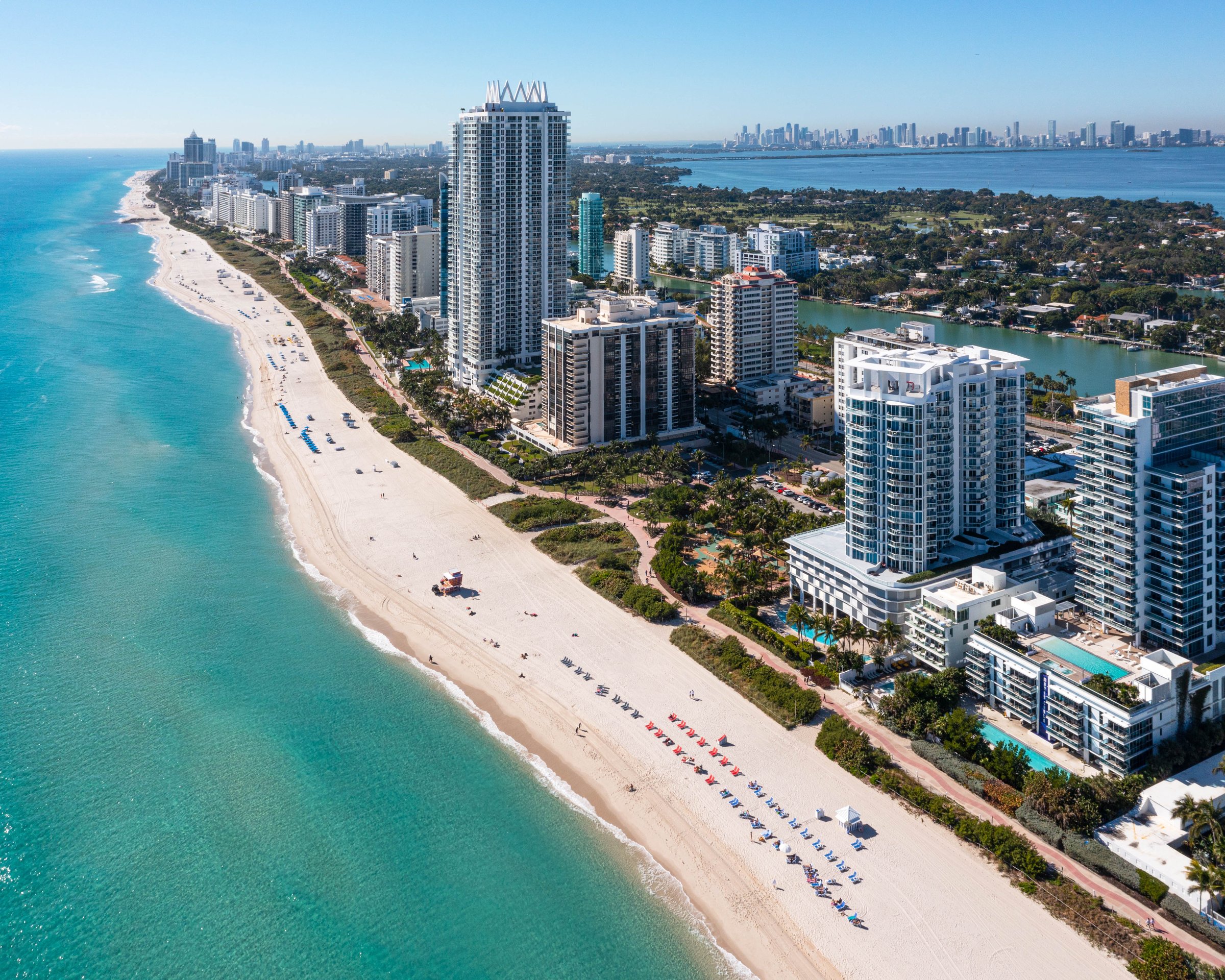 Aerial along the Miami Beach shoreline, surf breaking beside the palm-lined avenue north of the hotel
