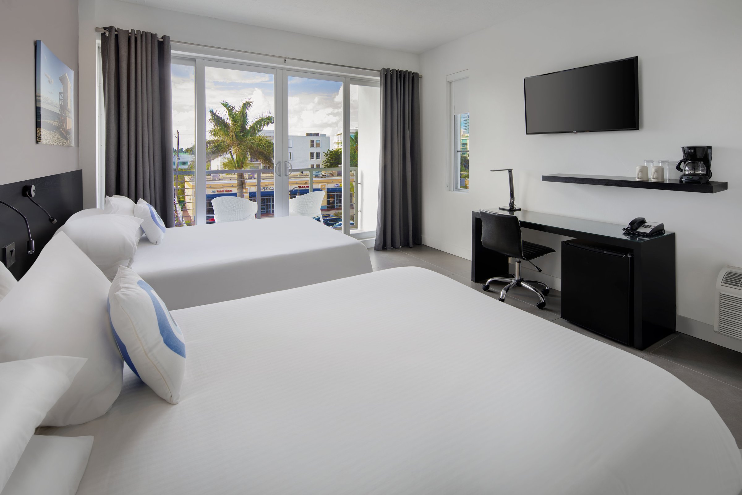 SNQ4 Deluxe Double Queen Suite — both beds with the desk, coffee service and television along the right-hand wall and the balcony doors open to a bright sky
