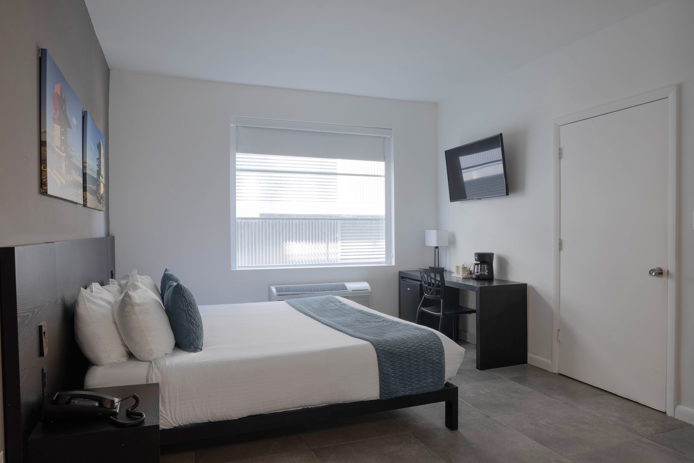 NK1 Standard King — king bed with a slate bed runner against a dark headboard, roller-shaded window at the centre of the room and a desk with coffee maker opposite