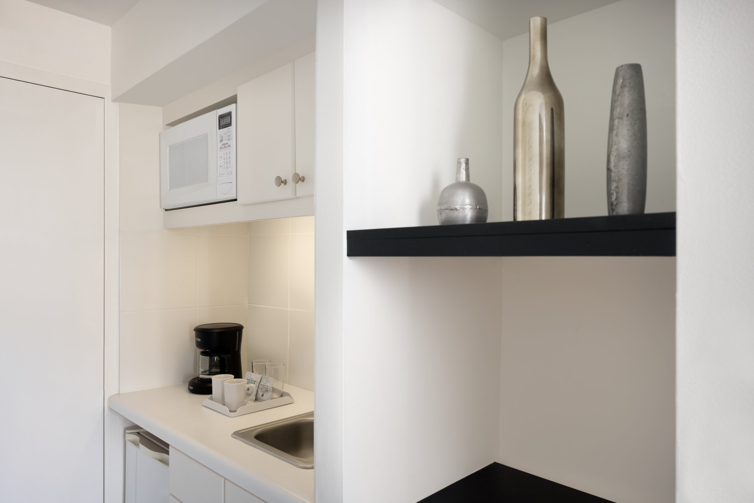 NK4 kitchenette from the room side — the counter and microwave alcove beside a black display shelf holding three metallic vases