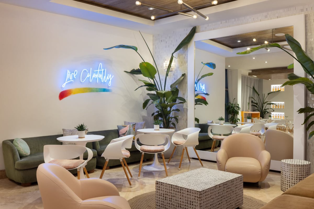 Lobby café seating beneath the 'Live Colorfully' neon, white tulip tables and cane chairs framed by bird-of-paradise palms
