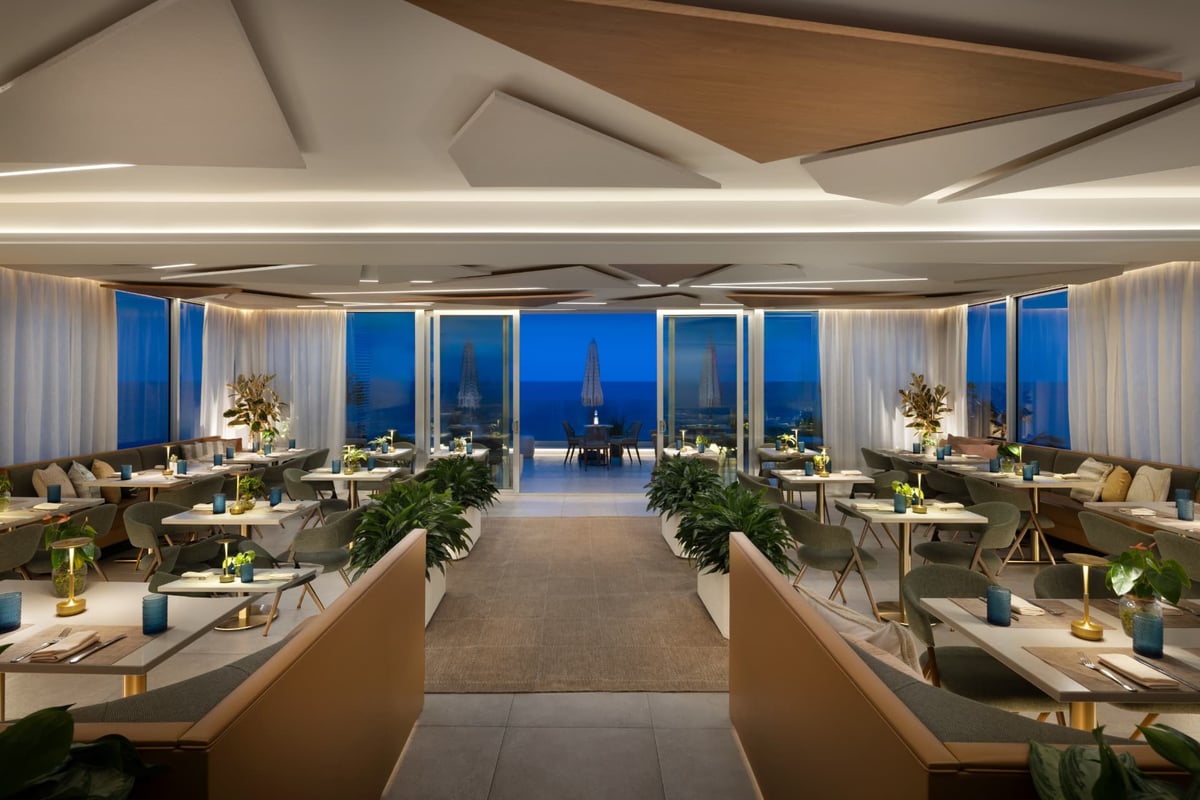 Kalypso at dusk, banquettes and blue glassware set for dinner as the ocean deepens beyond the windows