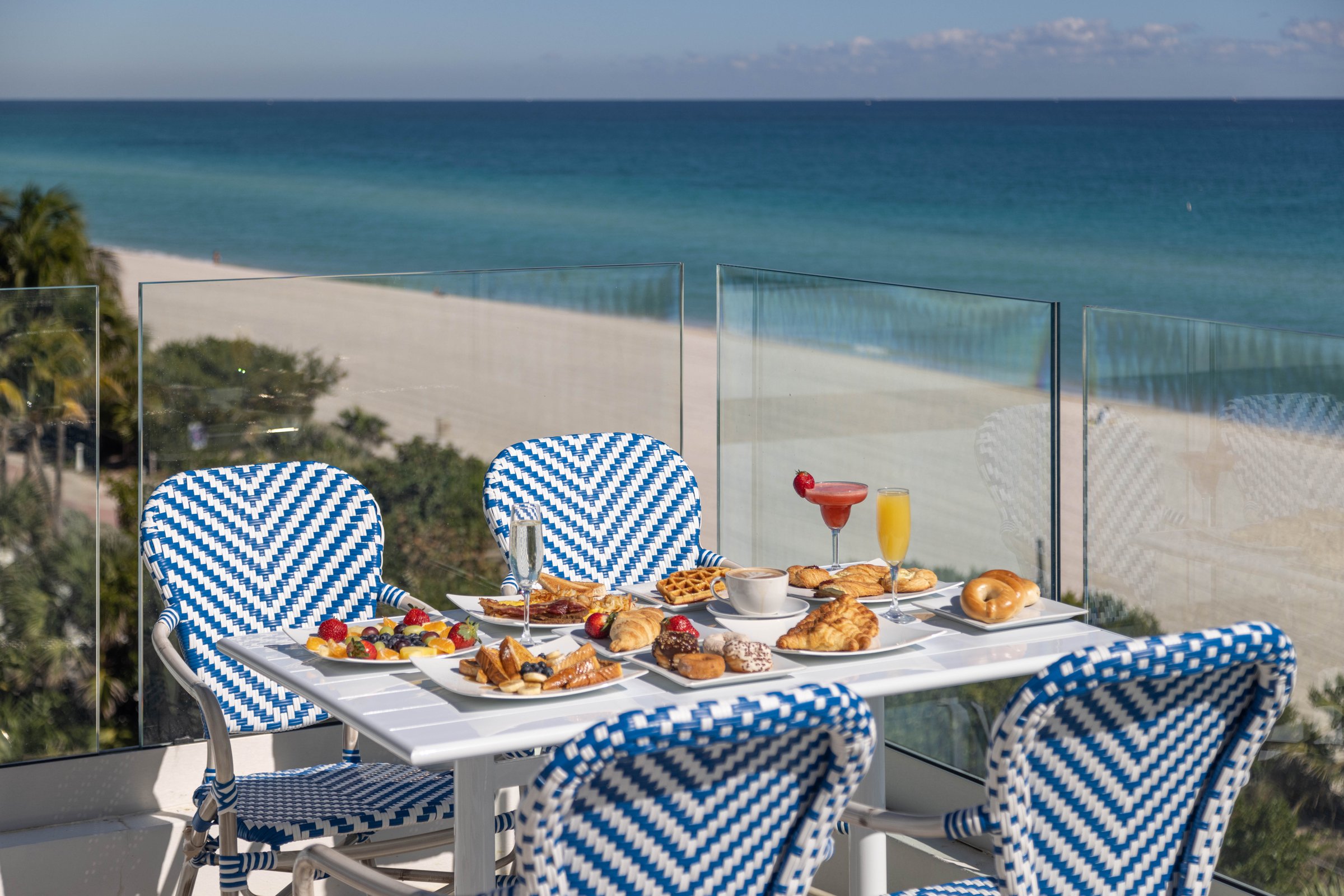 Breakfast on the MB Hotel rooftop — pastries, fruit and mimosas on a blue-and-white bistro table above the sand