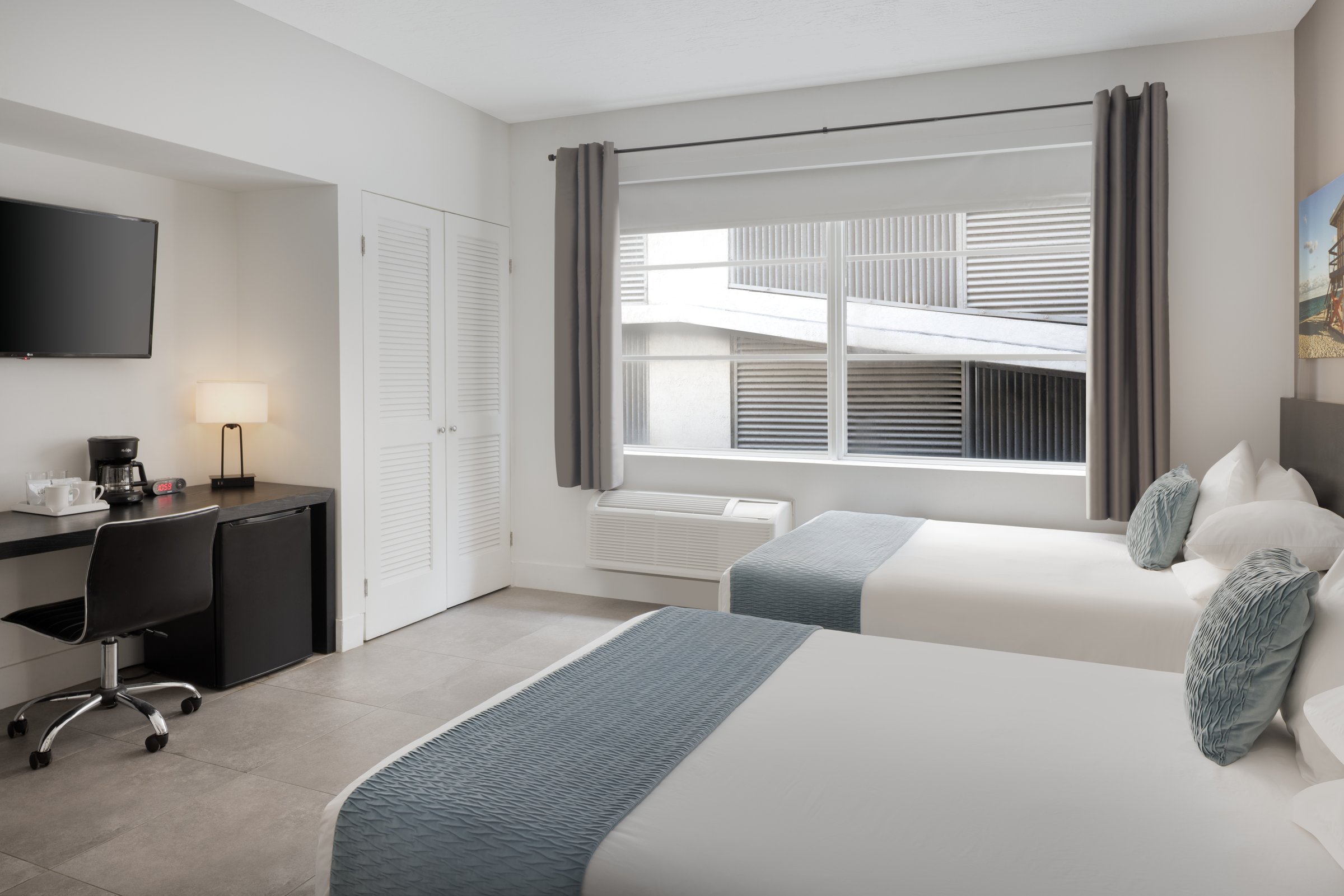 NDD1 Standard Double Full — two full beds with grey-blue bed runners beside a wide window, a black desk with coffee maker and cooler along the near wall