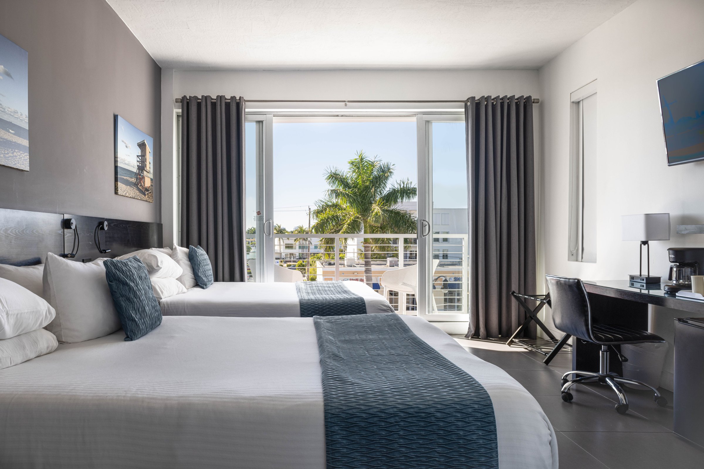 SNQ4 Deluxe Double Queen Suite — two queen beds beside open balcony doors framing a tall royal palm