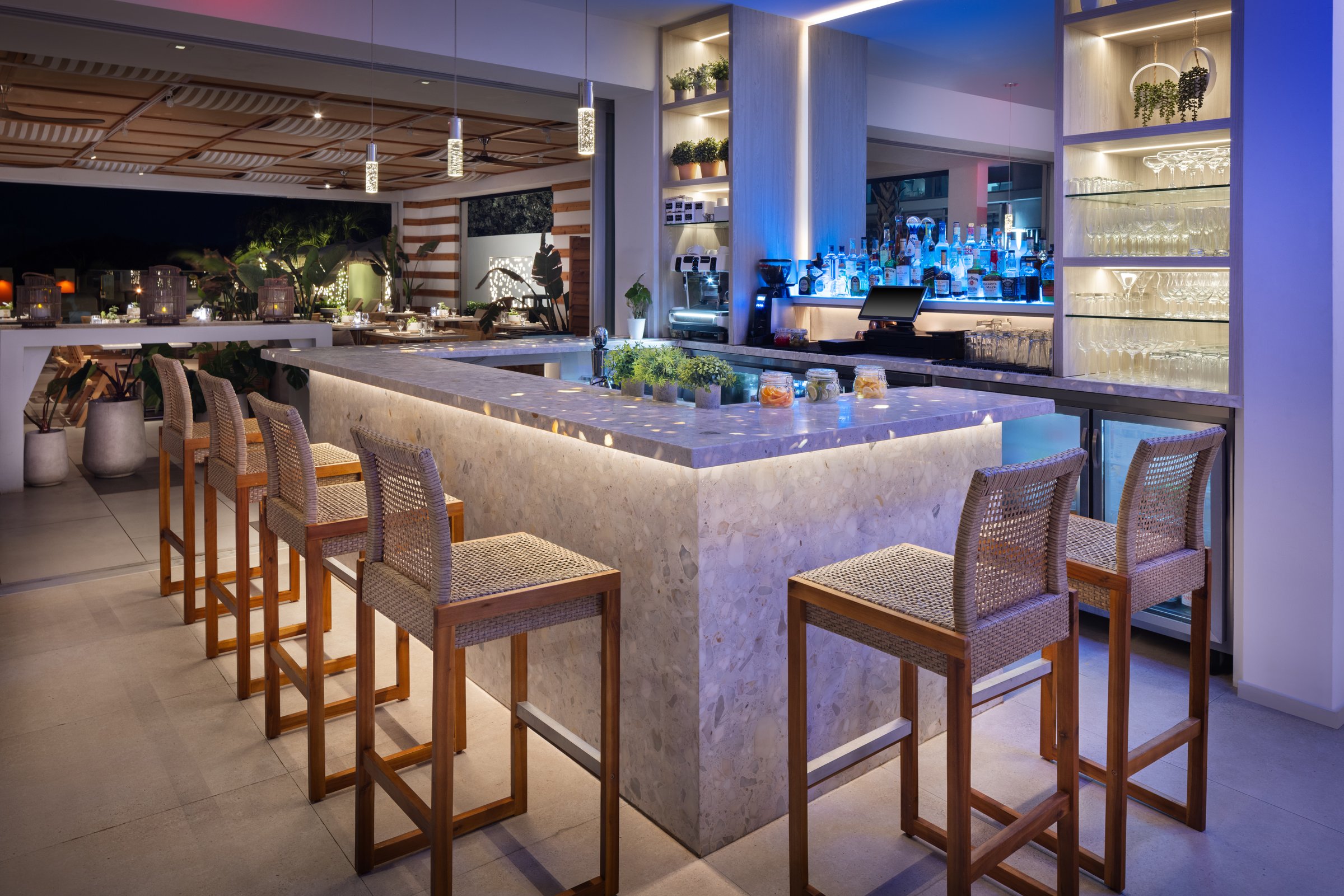 Kalypso terrazzo bar counter with woven stools and backlit glassware shelves
